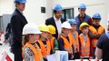Vivere una giornata in cantiere Bambini con caschi protettivi e giubbotti arancioni a una dimostrazione edilizia con adulti