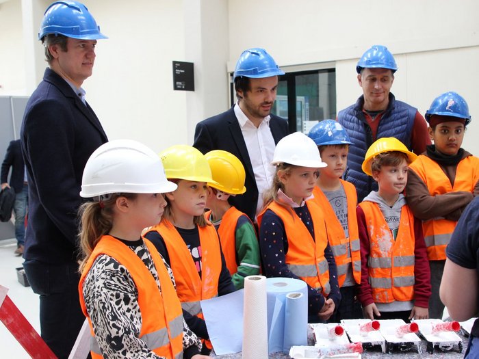 Vivere una giornata in cantiere Bambini con caschi protettivi e giubbotti arancioni a una dimostrazione edilizia con adulti