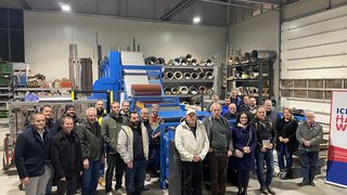 News Gruppenfoto von Erwachsenen in einer Werkstatt vor Maschinen und Materialregalen