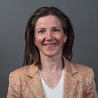 Maßschneider Porträt einer lächelnden Frau mit braunen Haaren vor grauem Hintergrund