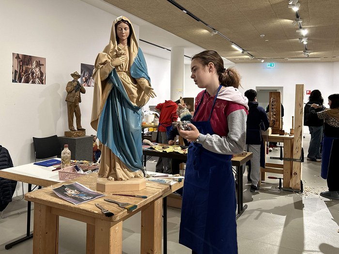 40 Betriebe, 100 Jugendliche, 15 Berufe Person malt eine große religiöse Statue in einem Workshop mit mehreren Teilnehmern