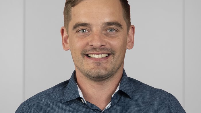 Kleine Betriebe als große Überlebenskünstler Porträt eines lächelnden Mannes in blauem Hemd vor neutralem Hintergrund