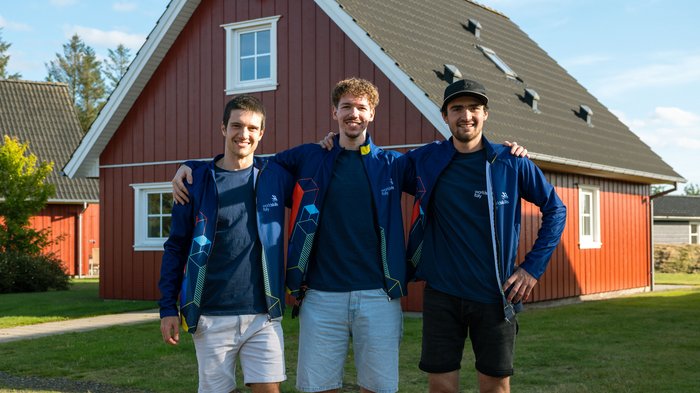 EuroSkills 2025: Südtirols Teilnehmer starten in den Wettbewerb Drei junge Männer mit blauen Jacken posieren vor einem roten Haus im Freien