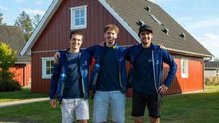 News Tre giovani uomini con giacche blu posano davanti a una casa rossa all'aperto