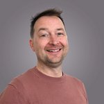 Das lvh-Team Lächelnder Mann mit braunem Pullover vor grauem Hintergrund