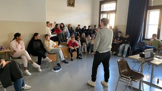 News Junger Mann hält Vortrag vor einer Gruppe von Jugendlichen in einem Klassenraum