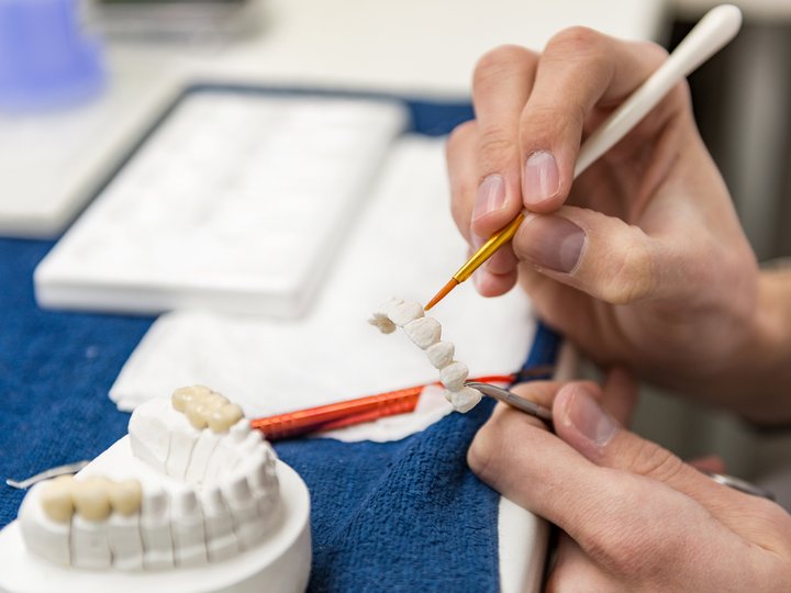 Odontotecnici Tecnico dentale dipinge ponte dentale con pennello fine in laboratorio