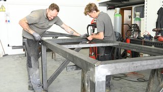 News Zwei Männer arbeiten an einem Metallrahmen in einer Werkstatt