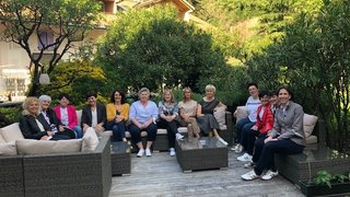News Gruppe von Frauen sitzt auf Gartenmöbeln im Freien neben Bäumen und Bergen