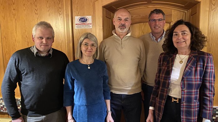 Riunione del gruppo comunale di lvh.apa a Bronzolo: bilancio del 2024 e prospettive per le iniziative future Cinque persone stanno in piedi davanti a una parete di legno in una stanza accogliente