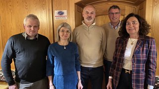 News Fünf Personen stehen vor einer Holzwand in einem Raum mit gemütlicher Atmosphäre