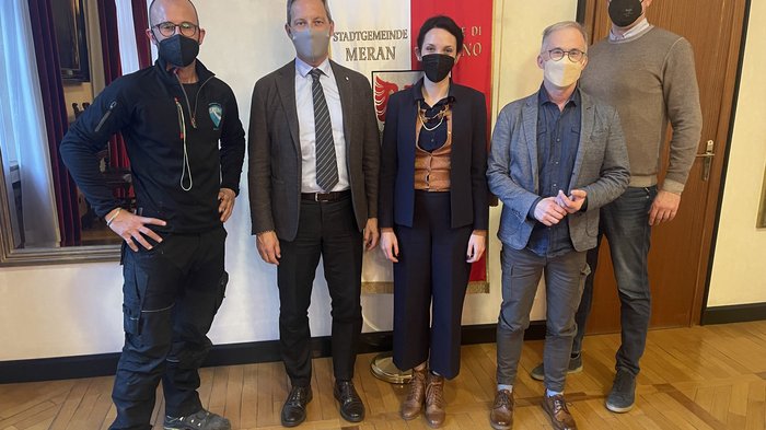 Meraner Handwerk trifft Meraner Gemeinde Fünf Personen mit Masken vor Stadt Meran Bannern in Büro