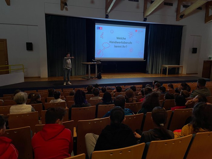 Mittelschule Mals: Jugendliche entdecken Berufe im Handwerk und Gastgewerbe Vortrag über handwerkliche Berufe vor einem Publikum in einem Saal