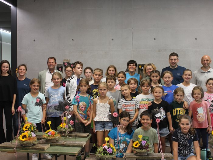 Blütenzauber und Gartenpracht: Das große Finale der KidsAcademy findet in Laimburg-Pfatten statt Gruppenfoto von Kindern mit ihren Blumenarrangements und Betreuern an der Wand