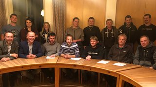 News Gruppenfoto von 15 Personen in einem Raum mit halbkreisförmigem Holztisch