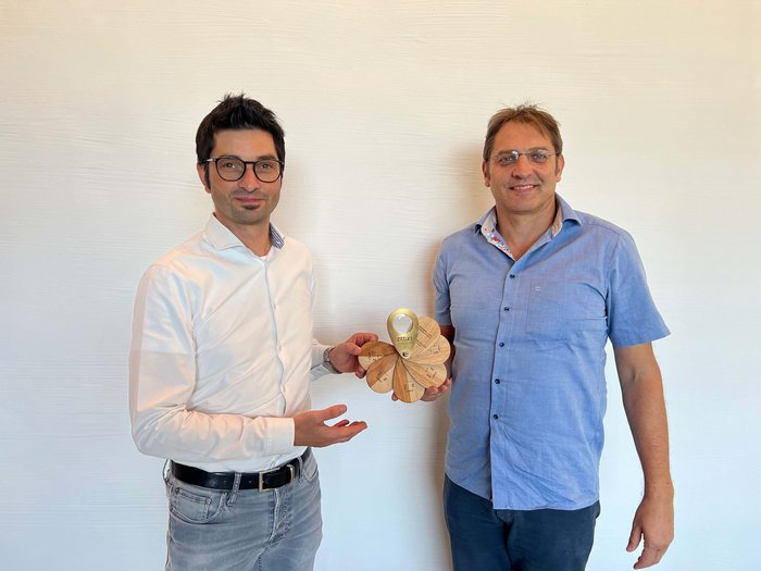 © Studiooberhauser Zwei Männer präsentieren ein hölzernes fächerförmiges Produkt vor weißer Wand