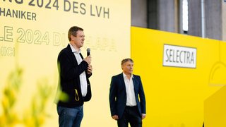 News Zwei Männer sprechen auf einer Veranstaltung vor gelbem Hintergrund mit Selectra-Logo