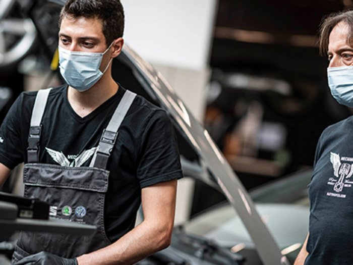 Prioritäten setzen und Lehrlingen eine Chance geben Zwei Mechaniker mit Masken arbeiten in einer Werkstatt am Auto.