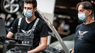 News Zwei Mechaniker mit Masken arbeiten in einer Werkstatt am Auto.