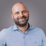 Das lvh-Team Porträt eines lächelnden Mannes mit Bart und blauem Hemd vor grauem Hintergrund