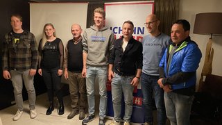 News Sieben Personen stehen nebeneinander vor Bannern in einem Raum