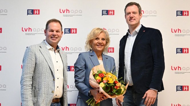 Home Tre persone posano davanti a sfondo con loghi, una tiene un mazzo di fiori