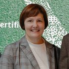 Das Nachhaltigkeitslabel Südtirol Frau in kariertem Blazer vor grünem Hintergrund mit weißem Muster