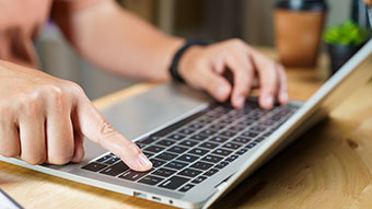 Konformitätserklärung Hand tippt auf Laptop-Tastatur auf Holztisch