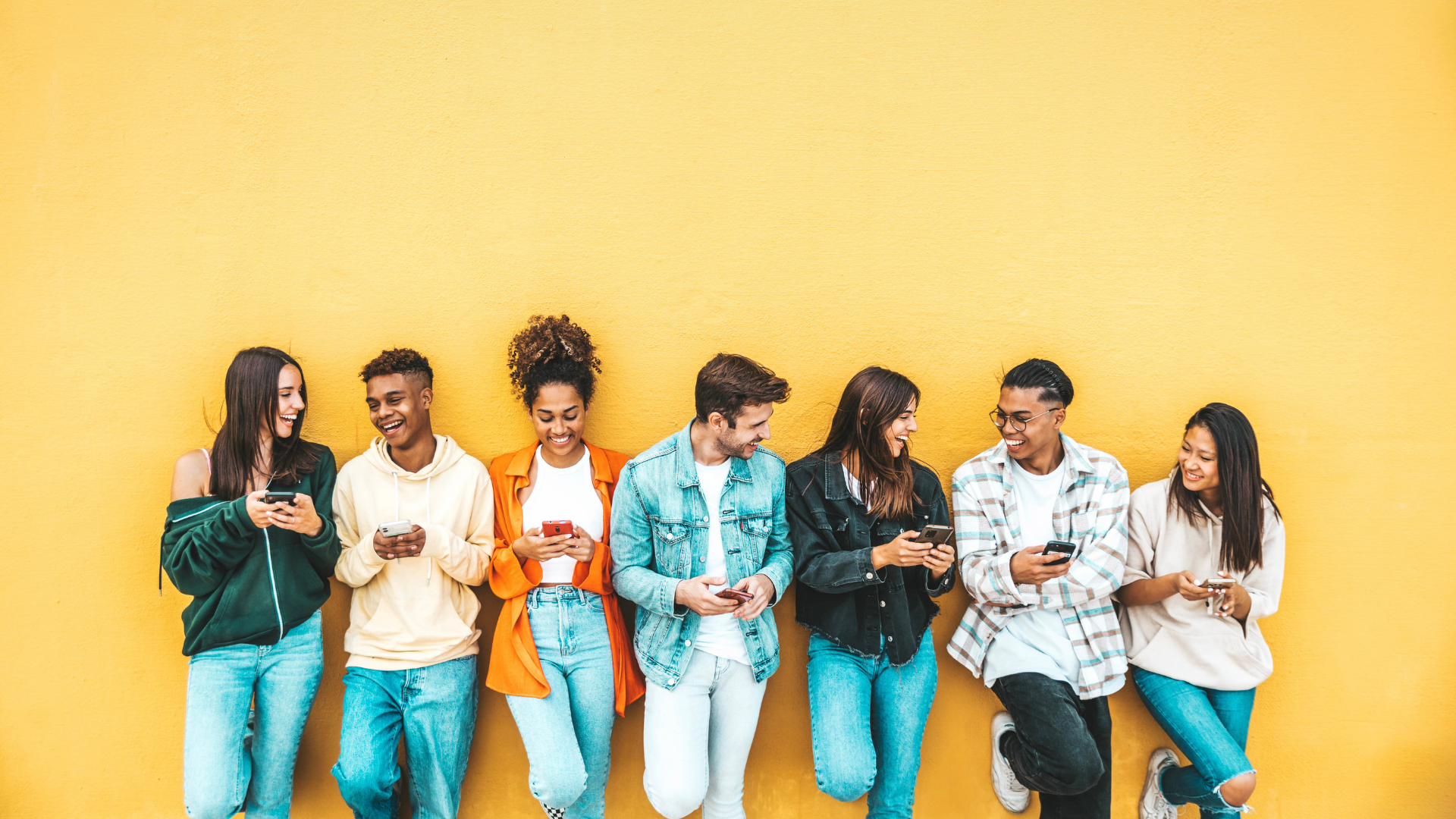 Home Giovani appoggiati a muro giallo che usano smartphone e ridono